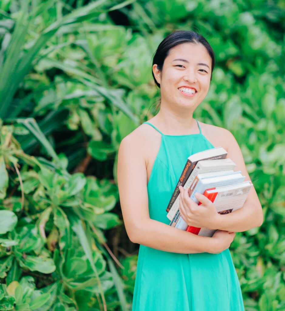 Real-life Wysa user smiling holding books with greenery in the background. Online therapy. Text-based therapy. Human coaching.