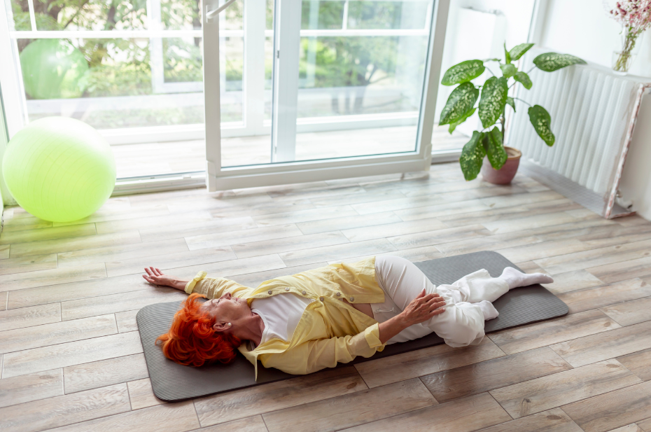 Older lady in a lying down spinal twist yoga pose to stretch the back and release stress and tension.