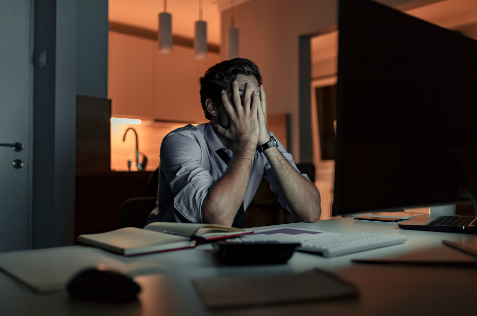 Man with hangs over face looking stressed while working from home late in the evening.