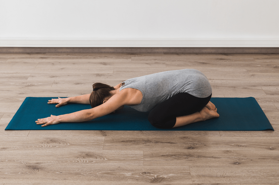 Woman on navy yoga mat in child's pose yoga pose releasing tension from her neck and shoulders to promote relaxation.